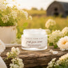 Fresh Face Cream anti-aging tallow moisturizer on wooden surface with flowers and greenery in a serene outdoor setting.
