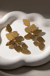 Gold statement dangle earrings with assorted geometric shapes on a white display. Perfect for making a bold statement.